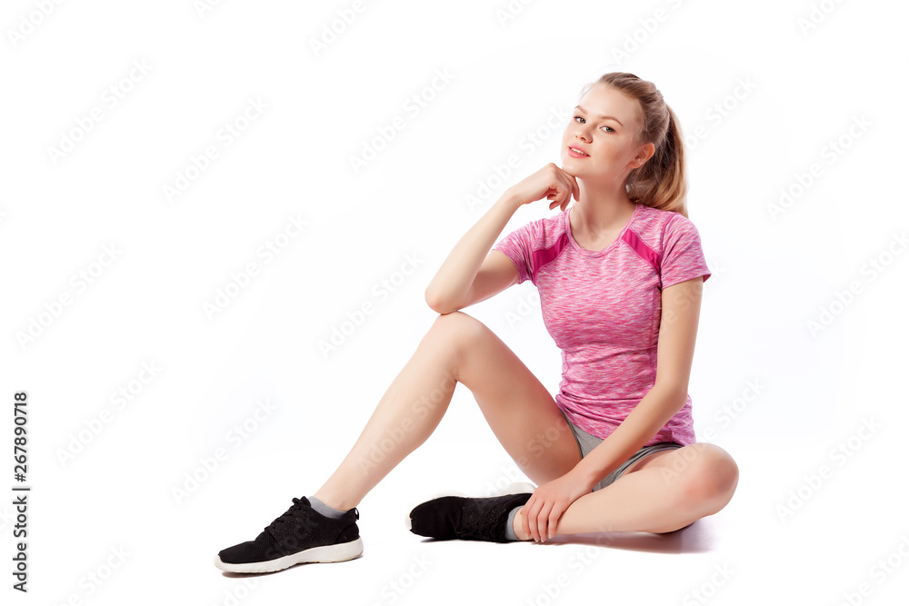 Young woman in sports clothes smilling, possing and sitting on the floor on white isolated background. Side view.Fit girl living an active lifestyle Young woman in sports clothes smilling, possing and sitting on the floor on white isolated background. Side view.Fit girl living an active lifestyle