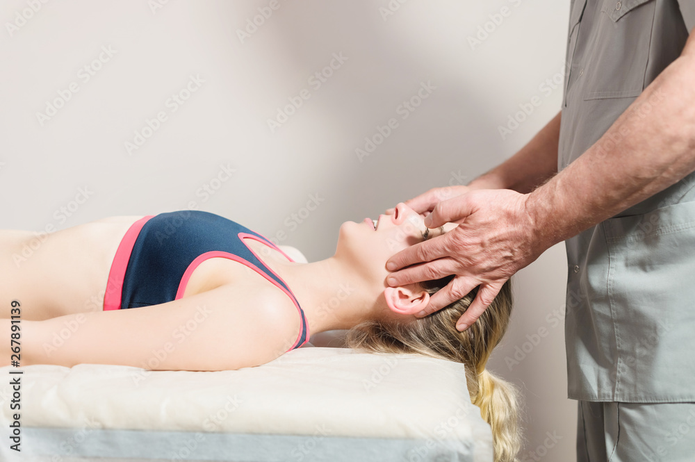 Male manual visceral therapist masseur treats a young female patient. Head and ear massage