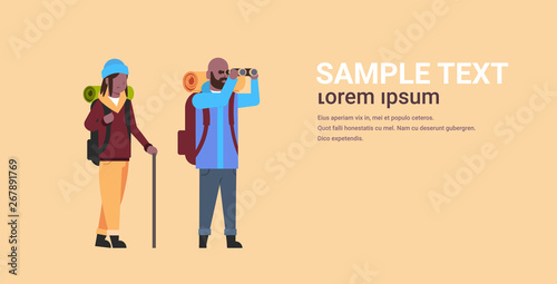 couple of tourists hikers with backpacks african american man looking through binoculars woman holding stick hiking concept travelers on hike horizontal full length copy space flat