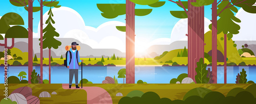 male tourist hiker with backpack african american man traveler holding stick standing in forest hiking concept sunrise landscape nature river mountains background horizontal full length