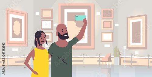 young couple taking selfie photo on smartphone camera african american man woman visitors in modern art gallery museum interior portrait horizontal