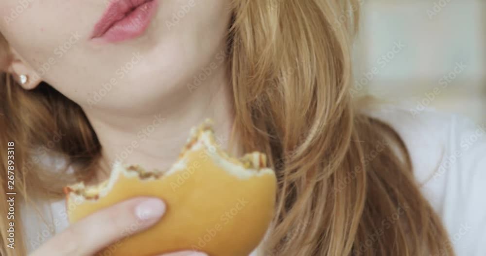 Unhealty food eating concept. Closeup face and mouth of young woman biting and chewing tasty burger.