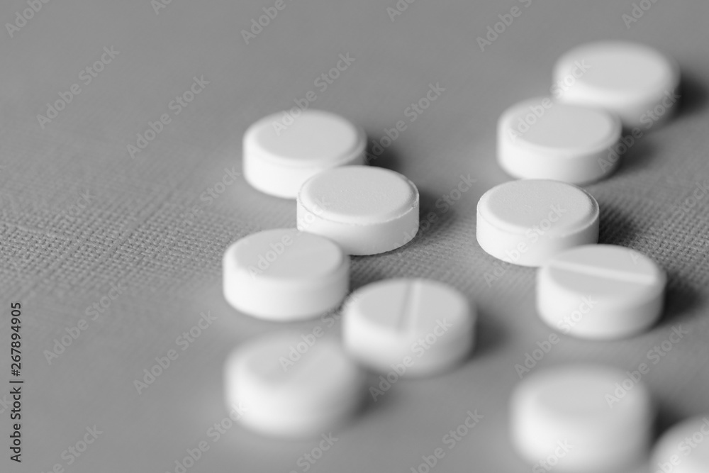 White tablets scattered on a gray surface close up. Black and white White tablets scattered on a gray surface close up. Black and white