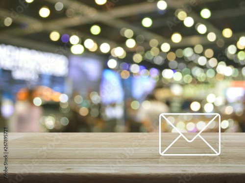 Mail icon on wooden table over blur light and shadow of shopping mall, Business contact us concept