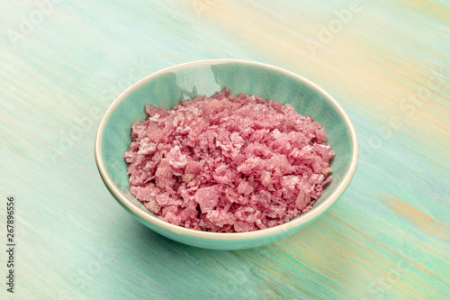 A bowl of pink Himalayan sea salt on a teal blue background