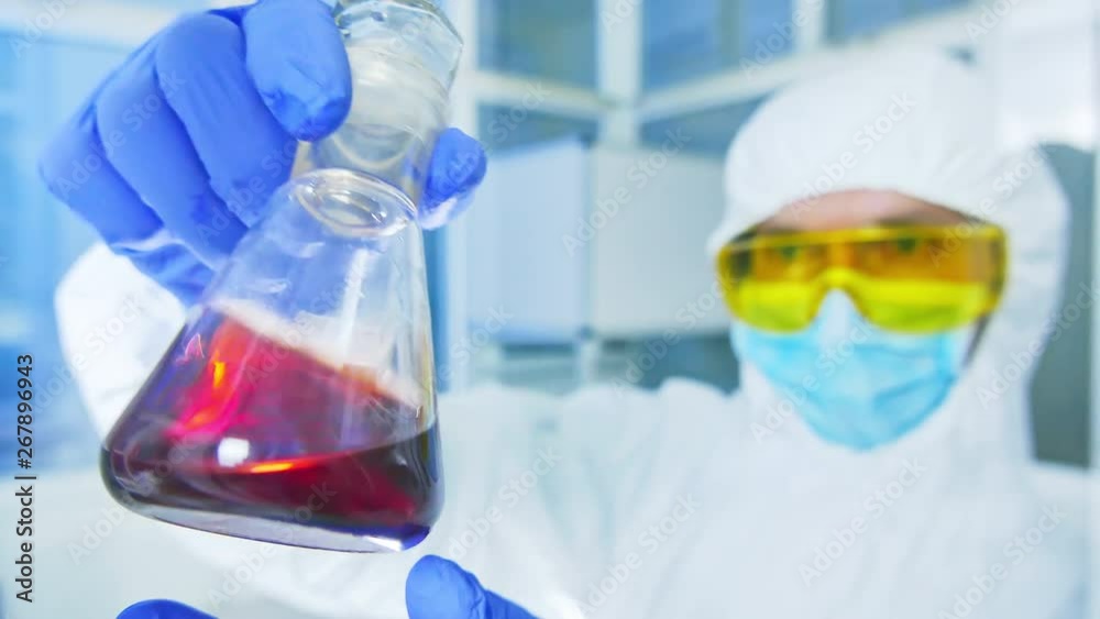Chemistry lab - Scientist in protective suit analyzing a liquid in laboratory flask Chemistry lab - Scientist in protective suit analyzing a liquid in laboratory flask