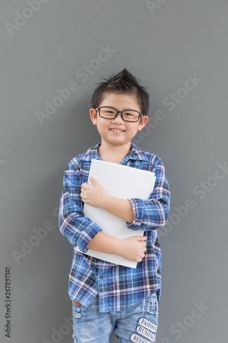 Asian boy feels happiness when time to school and his hands hold the book against the gray wall