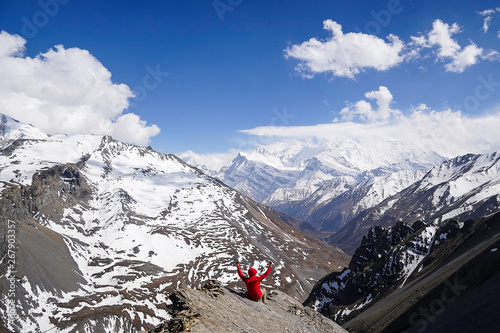 Achiement concept: Man wearing red jacket seating on the edge of a clift in Thorong-La Base Camp located in Annapurna Circuit