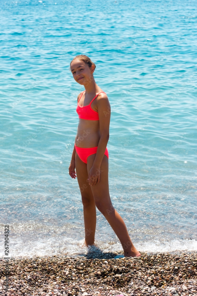 Pretty young girl in bikini standing on the beach near by sea
