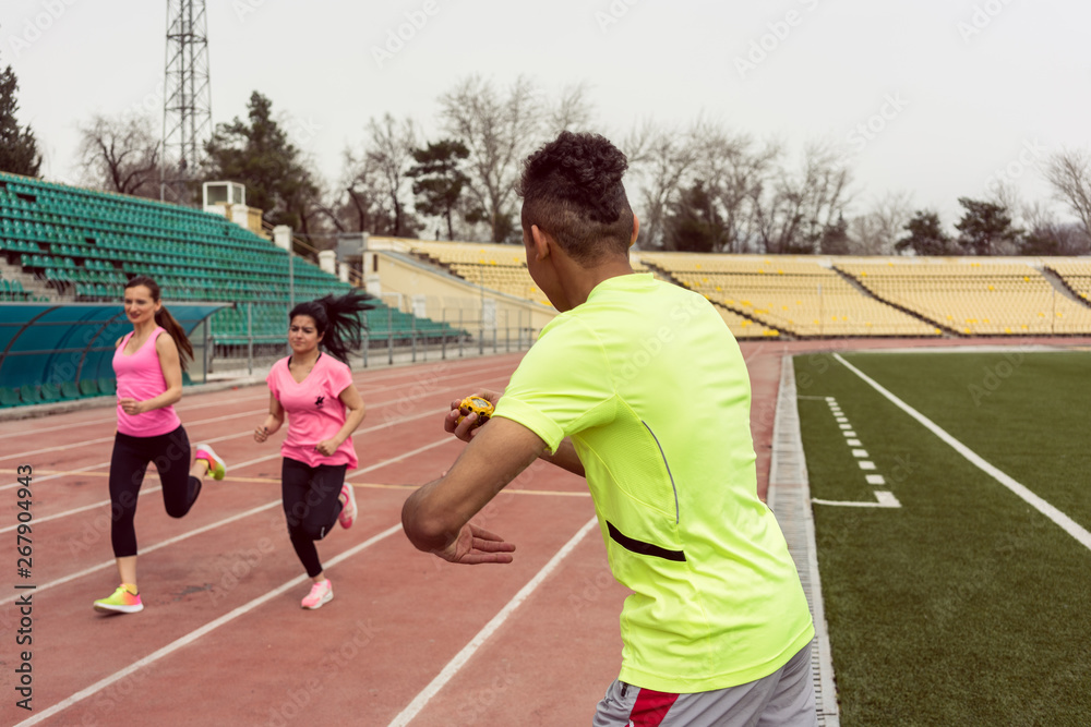 Man holding stop watch while women running Man holding stop watch while women running