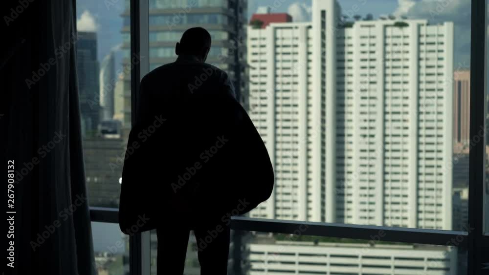 Young businessman taking off jacket on by window at home Young businessman taking off jacket on by window at home