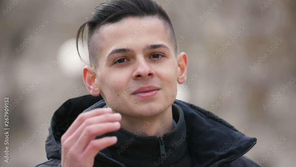 Cheery young man putting his hair in order outdoors in spring in slow motion Cheery young man putting his hair in order outdoors in spring in slow motion