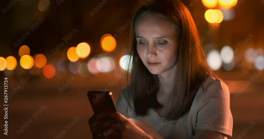 Bokeh night city young woman looking into smartphone screen Bokeh night city young woman looking into smartphone screen