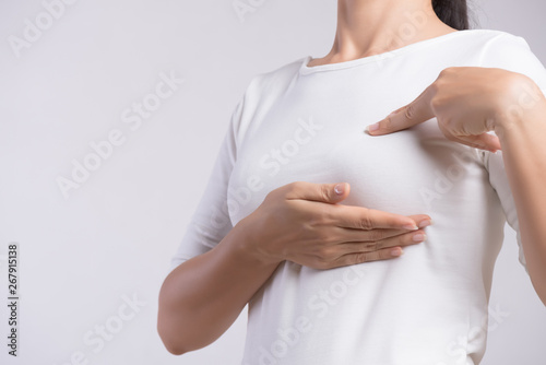 Woman hand checking lumps on her breast for signs of breast cancer on gray background. Healthcare concept. photo
