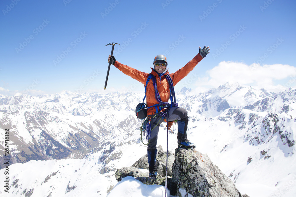 mountaineer with ice ax stands on the top of a mountain in the background of the landscape of snowy mountains