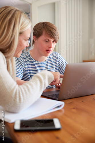 Downs Syndrome Man Sitting With Home Tutor Using Laptop For Lesson At Home