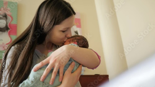 Young mother holds and kiss taking care charishing her newborn baby daughter in maternity hospital couple of days after birth photo