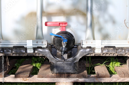 Additional small valve added to intermediate bulk container or IBC plastic water tank with metal cage put on wooden pallet in local garden on warm sunny spring day photo