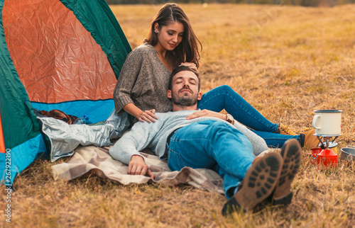 Happy young couple sitting by tent at campsite spending time together in nature.