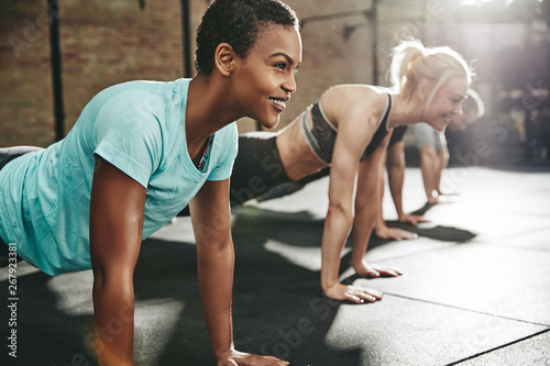 Smiling young woman doing pushups with friends at the gym