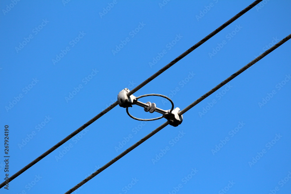 Two power line utility black electrical wires held together with strong insulators and spacers on clear blue sky background Two power line utility black electrical wires held together with strong insulators and spacers on clear blue sky background