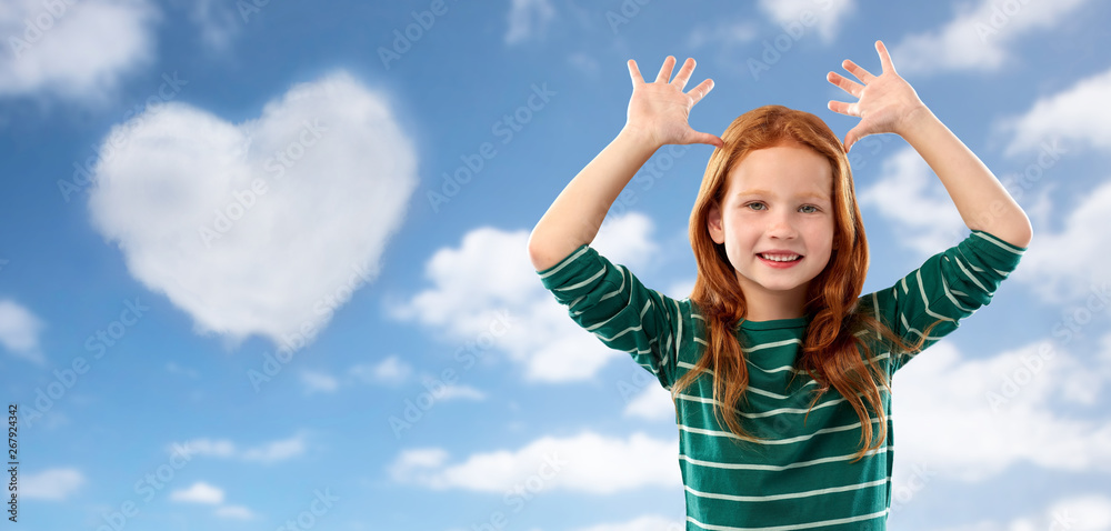 childhood, valentine's day and people concept - smiling red haired girl in green striped shirt having fun and making big ears over blue sky and heart shaped cloud clouds background childhood, valentine's day and people concept - smiling red haired girl in green striped shirt having fun and making big ears over blue sky and heart shaped cloud clouds background