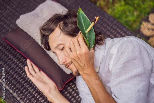 man having an ear candle therapy against the backdrop of a tropical garden photo