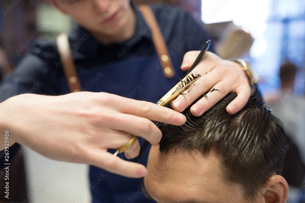 Fototapeta premium grooming, hairdressing and people concept - close up of male client and hairdresser with comb and scissors cutting hair at barbershop