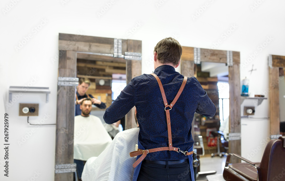 grooming, hairdressing and people concept - hairdresser cutting male client's hair at barbershop
