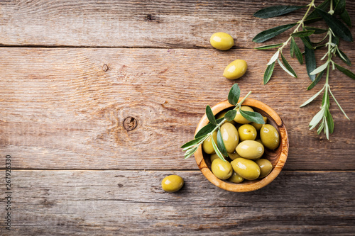 Foto Fresh green olives in a bowl and olive branch on rustic wooden background, top v