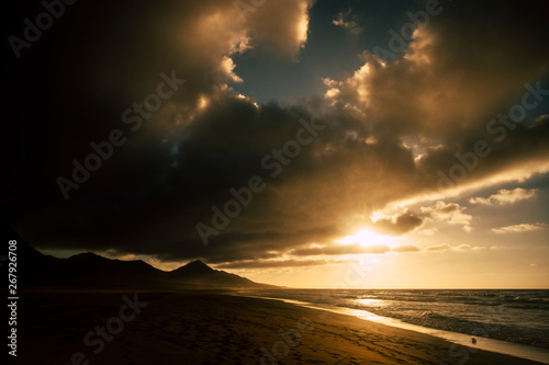 Dramatic dark shadows sunset at the beach with black mountains in background - sun and ocean for adventure concept - scenic landscape and beautiful sky with clouds