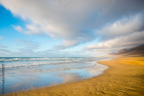 Summer solitary beach with water reflections concept - beautiful landscape with ocean and waves - blue sky and mountains in backgrund - coloured hevan spot