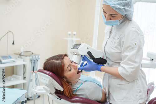 Attractive smiling woman doctor in a white uniform with tools in hand. Young beautiful female dentist takes jaw x-ray of female patient. Attractive woman patient at dentist taking x-ray exam.
