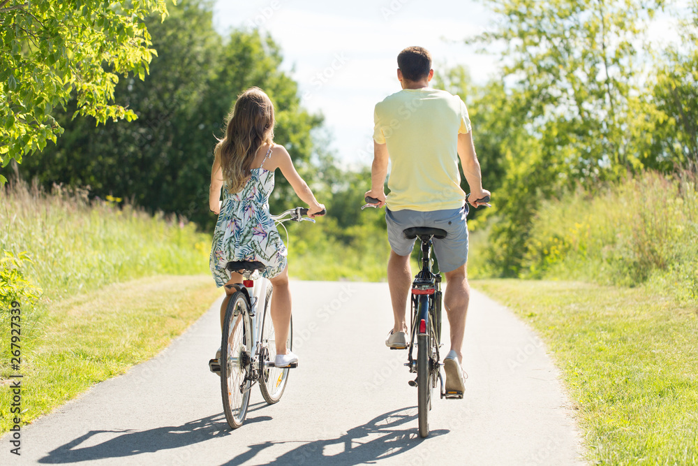 people, leisure and lifestyle concept - young couple riding bicycles along road in summer