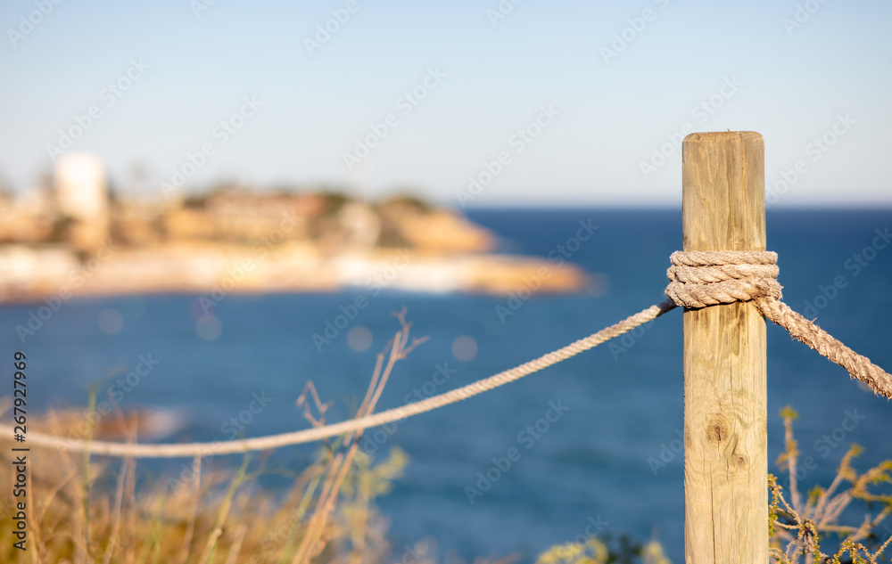 On an afternoon on the Mediterranean coast of Cabo Roig with a rope post standing on the edge of the high cliff overlooking the blue sea with beautiful bokeh.