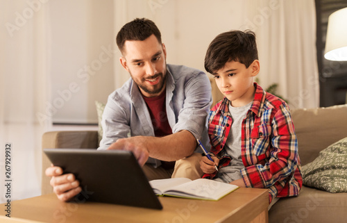 education, family and homework concept - happy father and son with tablet computer writing to notebook at home © Syda Productions