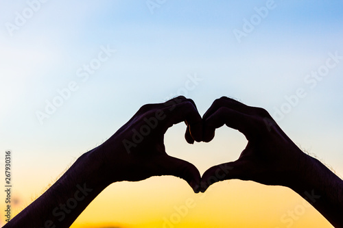 Love sign. Heart symbol by hand silhouette in sunset sky