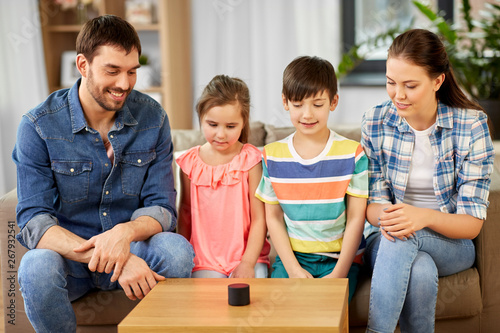 family, technology and internet of things concept - happy father, mother, little son and daughter with smart speaker at home