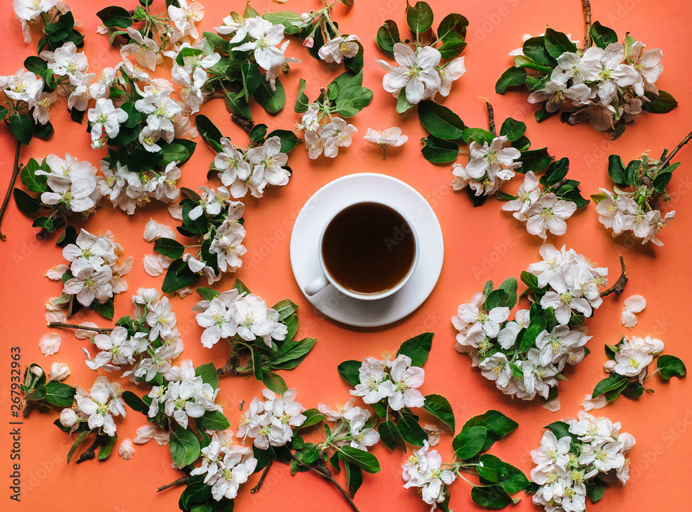 A cup of tea stands on a coral background surrounded by white flowers of an apple tree. The concept of spring tea and medicinal decoctions. Flat lay. A cup of tea stands on a coral background surrounded by white flowers of an apple tree. The concept of spring tea and medicinal decoctions. Flat lay.