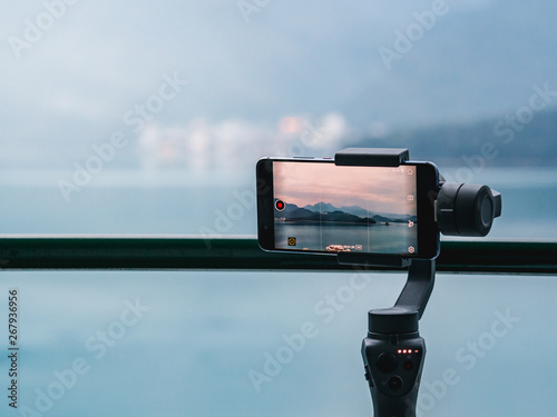 A gimbal stabilizer with mobile phone taking a timelapse of the mountain and lake landscape.