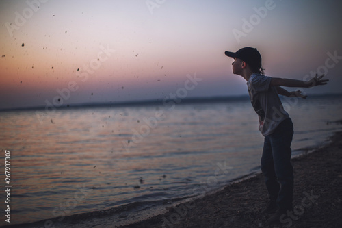 boy at sunset on the beach throws stones into the water
