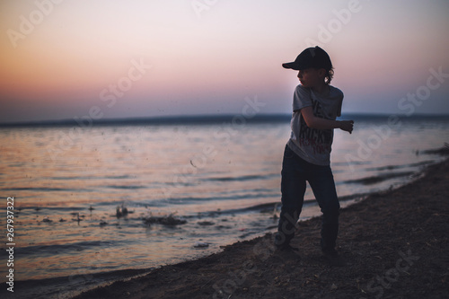 boy at sunset on the beach throws stones into the water