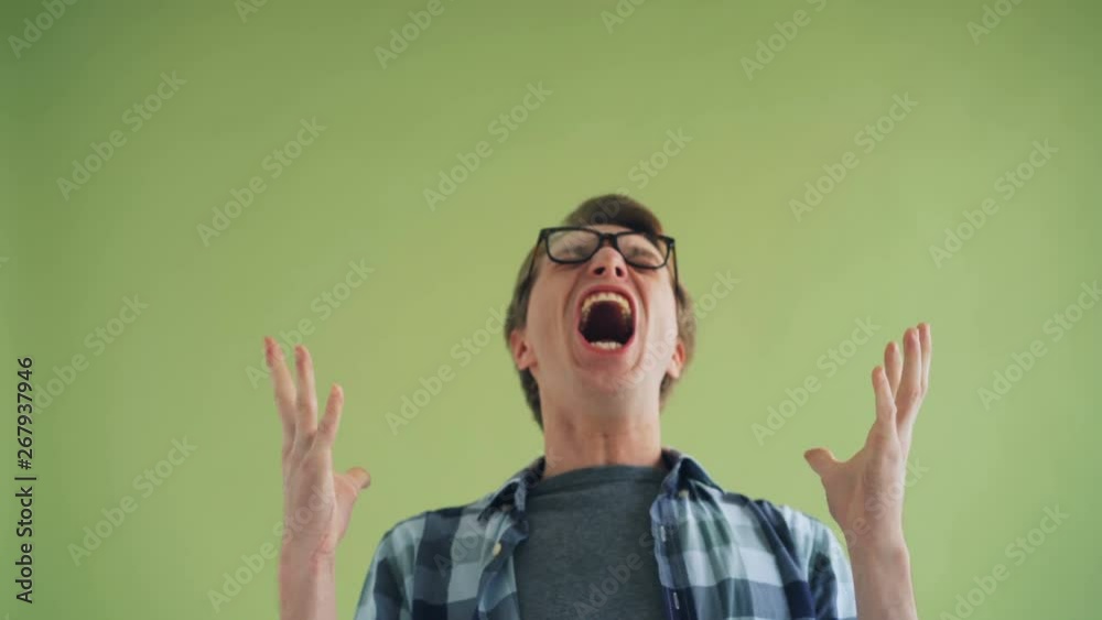Portrait of screaming young man mad hipster yelling standing alone on green background feeling irritated and distressed. Scream and negativity concept. Portrait of screaming young man mad hipster yelling standing alone on green background feeling irritated and distressed. Scream and negativity concept.
