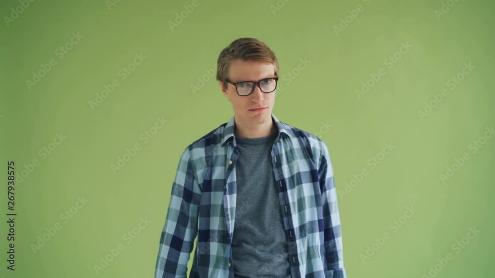 Portrait of disappointed young guy in trendy outfit showing thumbs-down and shaking head on green background. Unsatisfied people and emotions concept. Portrait of disappointed young guy in trendy outfit showing thumbs-down and shaking head on green background. Unsatisfied people and emotions concept.