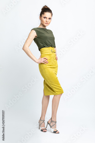 Model in green blouse, yellow suede skirt with yellow belt, white heeled sandals isolated on white background.