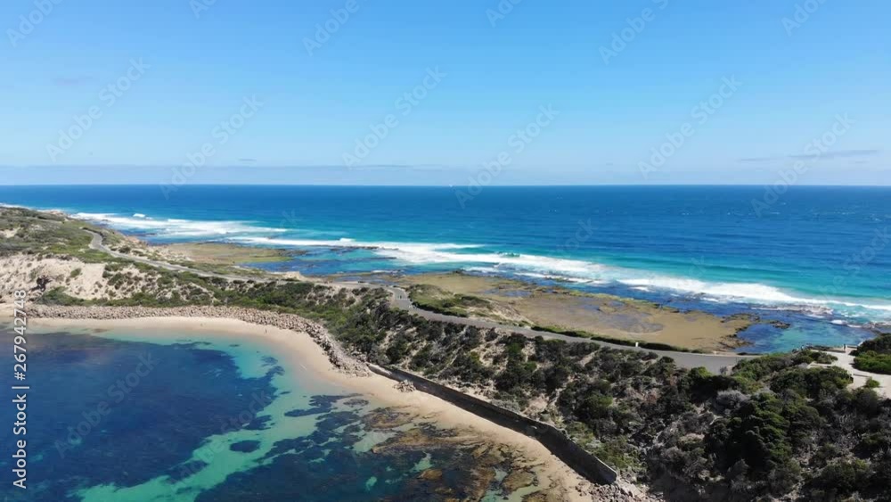 Slow aerial shot with pedestrians traveling along the road watching the waves crash against the beaches of the Nepean Peninsula Slow aerial shot with pedestrians traveling along the road watching the waves crash against the beaches of the Nepean Peninsula