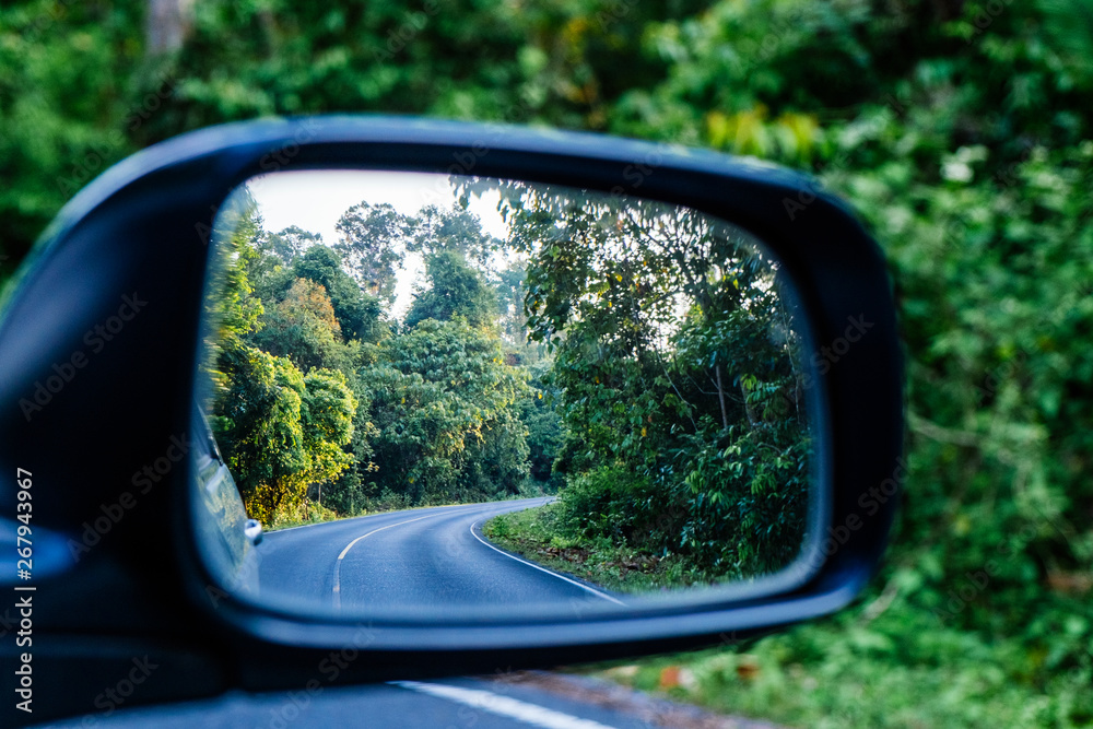 Side view mirror reflection of curve road in the forest.