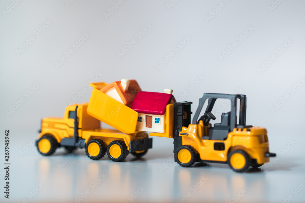 Miniature forklift truck lifting up mini house using as property real estate and industry concept Miniature forklift truck lifting up mini house using as property real estate and industry concept