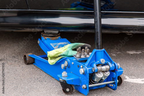 Blue jack raises the black car. Car repair in a car repair shop.