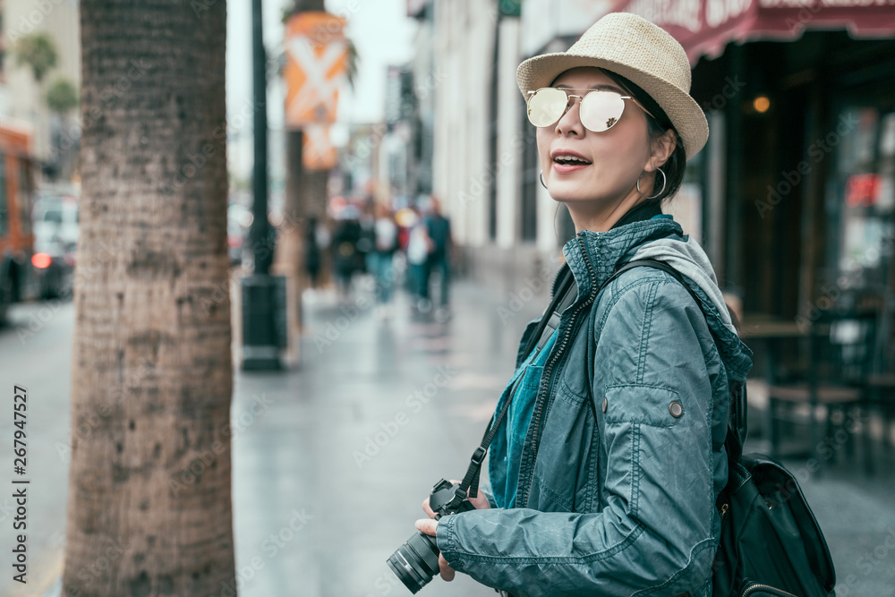 asian woman photographer traveler lifestyle concept. positive young girl backpacker in sunglasses holding professional camera standing on street of hollywood boulevard walk enjoy city view sunshine.